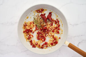 Adding spices and tomato paste to the skillet.