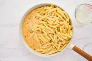 Adding cooked penne pasta to the cream sauce.