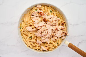 Stirring flaked salmon into the pasta.