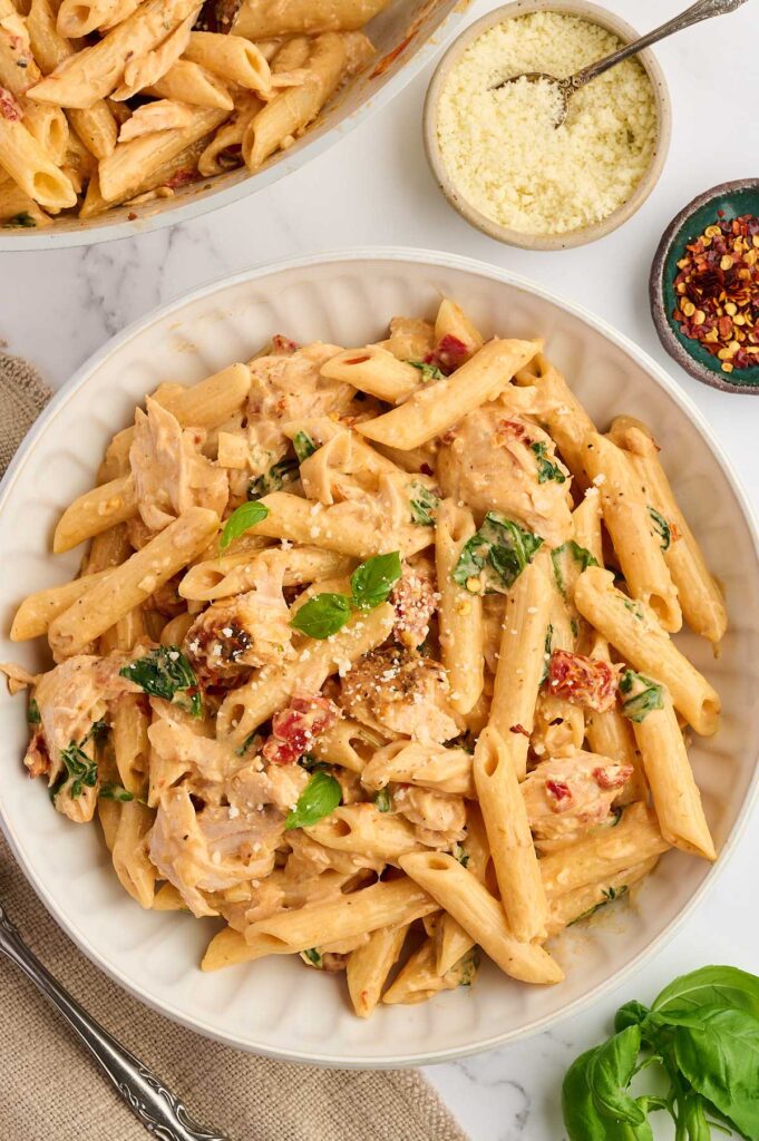 A bowl of salmon penne pasta next to a dish of parmesan cheese.