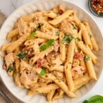 A bowl filled with salmon penne pasta topped with basil leaves.