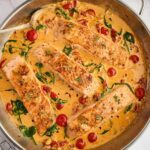 Salmon fillets in creamy spinach-tomato sauce, cooked in a skillet.