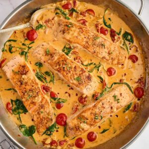 Salmon fillets in creamy spinach-tomato sauce, cooked in a skillet.
