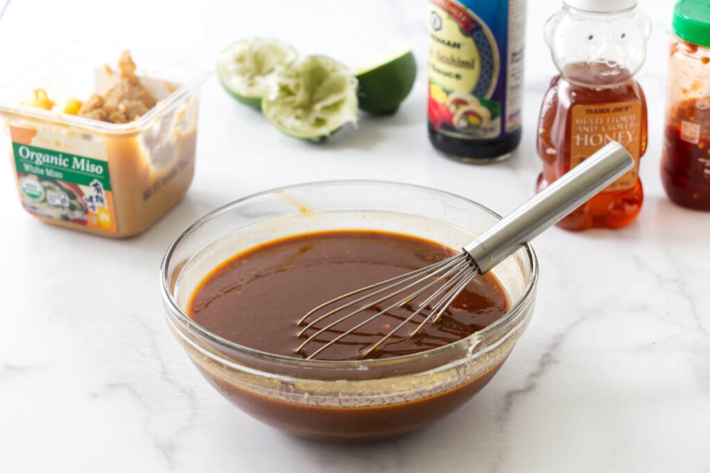 Glass bowl of miso glaze sauce being whisked, surrounded by various condiments.