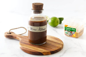 A glass bottle filled with homemade miso sauce in front of limes.