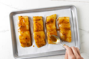 Drizzling miso marinade over halibut fillets on a sheet pan.