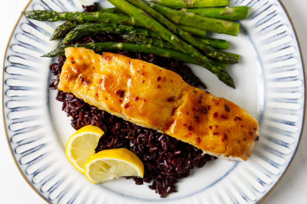 A serving of miso halibut on a plate with black rice and asparagus.