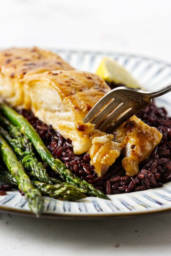 A fork flaking off a serving of halibut.