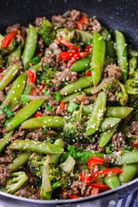 Close-up of ground beef stir fry with snap peas, broccoli, peppers, and sesame seeds.