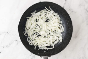 Sliced onions in a skillet for the start of a ground beef stir fry.