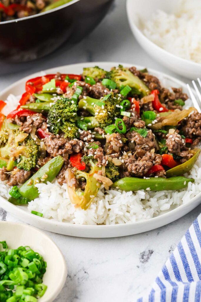 Easy ground beef stir fry spooned over rice with green onions on top.