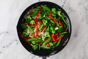 Vegetables for ground beef stir fry cooking in a skillet before the beef is added.