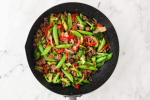 Ground beef stir fry with broccoli, snap peas, and red bell pepper in a skillet.