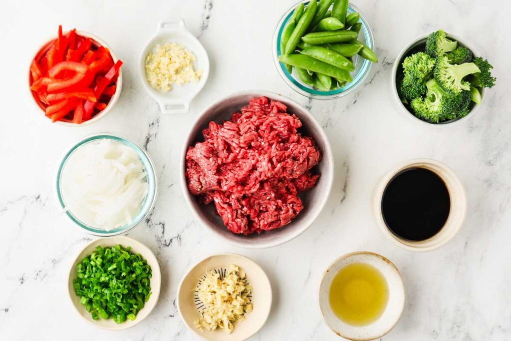 Ingredients for a ground beef stir fry recipe arranged on a marble counter.