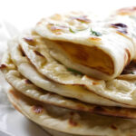 Stack of fresh naan bread, one piece folded to show its texture.