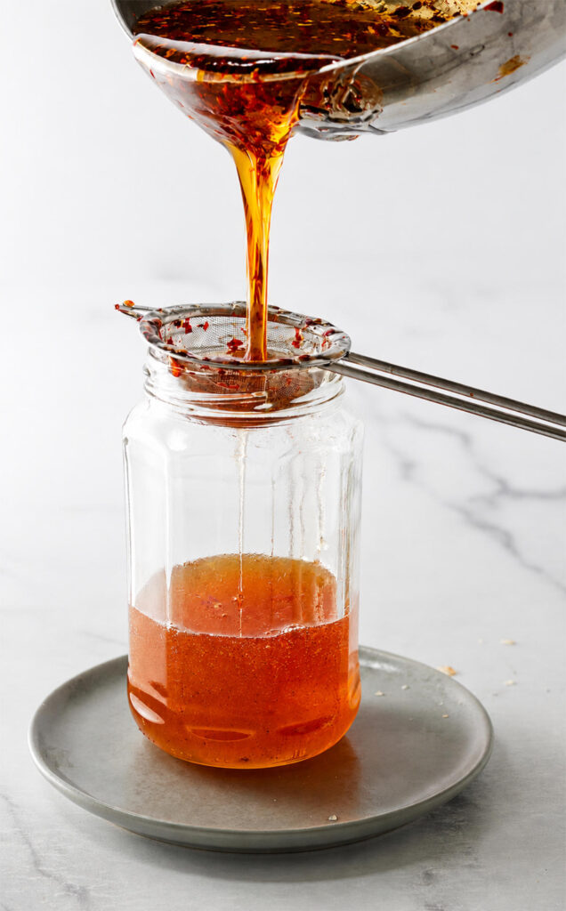Pouring warm spicy honey through a strainer.