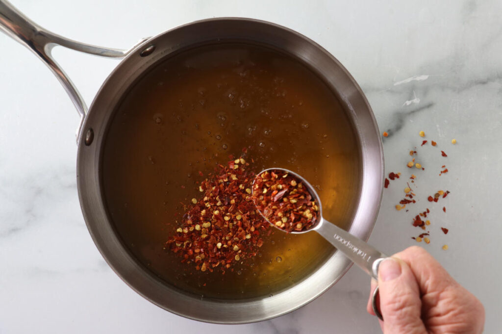 Adding chili pepper flakes to a skillet of hot honey.