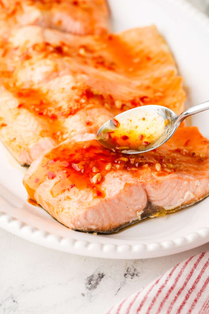 Spoon drizzles chili garlic honey sauce over salmon fillets on a white plate.
