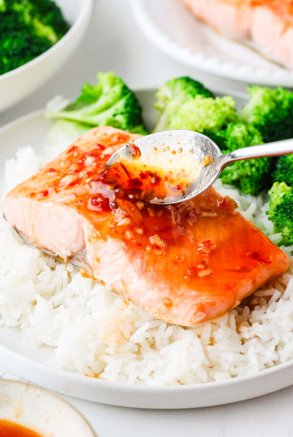 A spoon drizzling sweet and spicy sauce over a salmon fillet.