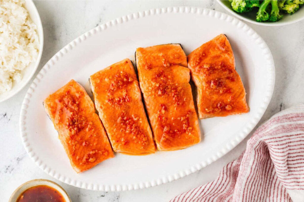 A spicy honey sauce on top of four salmon fillets on a white platter.