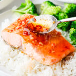 A spoon drizzling spicy honey sauce over a salmon fillet.