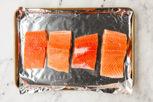 Four salmon fillets on a sheet pan.