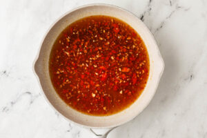 A skillet with hot honey sauce on a marble counter.
