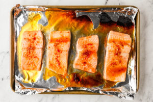 Four salmon fillets on a sheet pan topped with caramelized hot honey sauce.