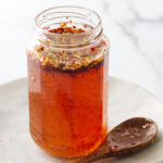Hot spicy honey in a jar next to a spoon.