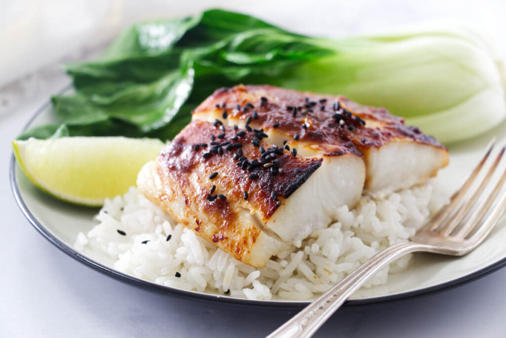 Miso sea bass on a bed of rice with lime and bok choy in the background.