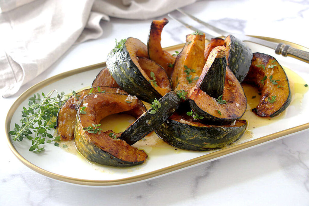 Roasted kabocha squash wedges with herbs on a white plate.