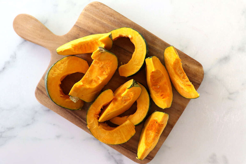 Slices of raw kabocha squash on a small wooden cutting board.