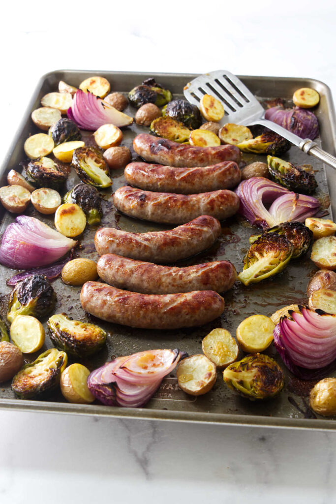 A baking tray with roasted sausage and vegetables on a counter.