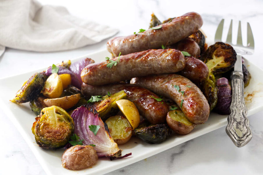 Roasted sausages on potatoes, Brussels sprouts, and onions, garnished with parsley.