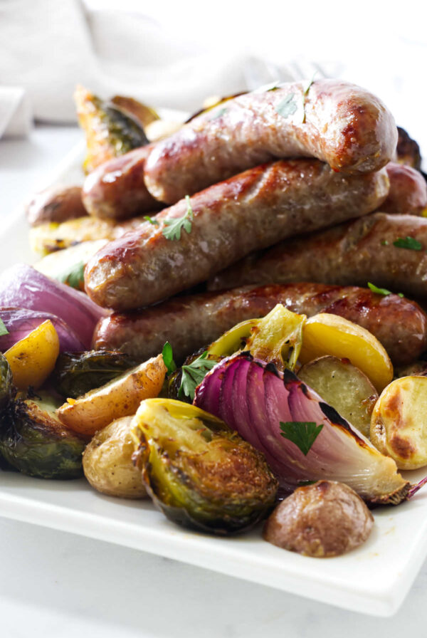 Roasted sausages on a bed of assorted vegetables, garnished with parsley.