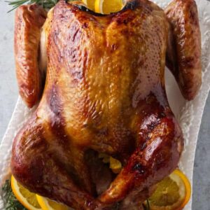 Smoked turkey on platter with rosemary, orange slices, and gravy pitcher.