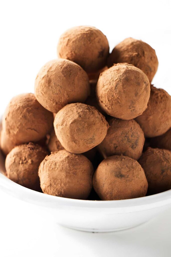 Chocolate truffles coated in cocoa powder piled in a white bowl.