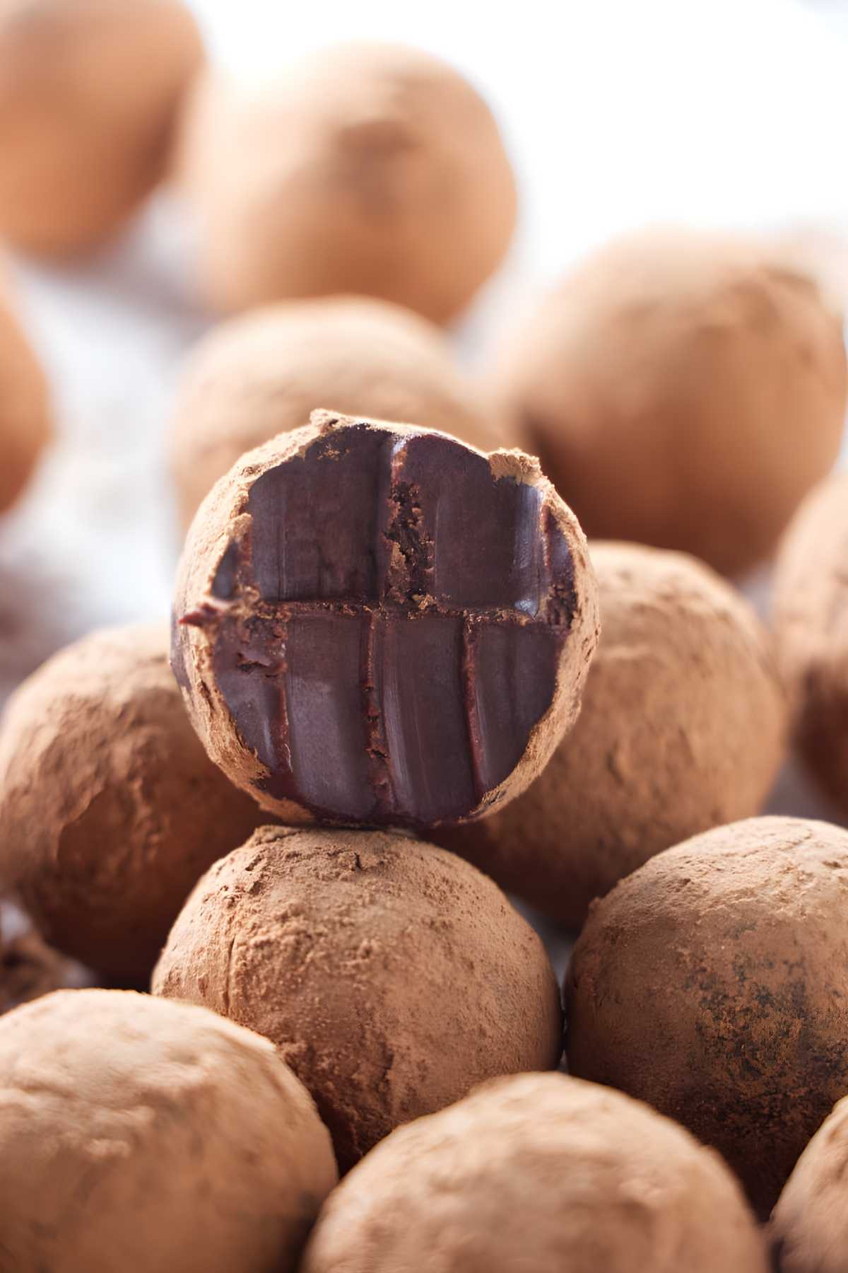 Chocolate truffles dusted with cocoa, one cut to reveal dark filling.