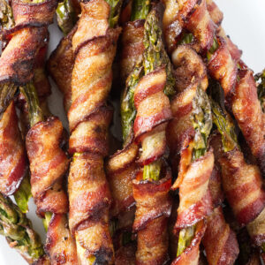 Asparagus spears wrapped in bacon on a white platter.
