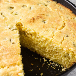 Cornbread with jalape&ntilde;os in skillet, one slice removed showing moist inside.