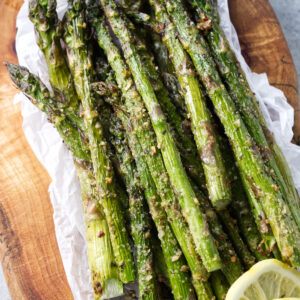 Several smoked asparagus spears on a serving board with lemon slices.