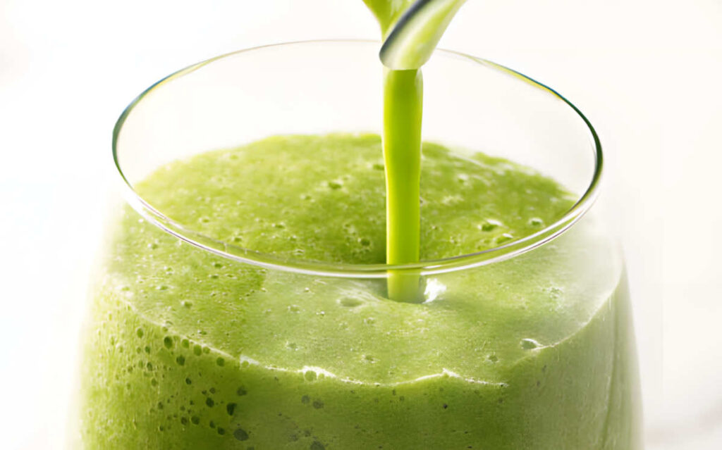 Pouring a green arugula drink into a glass.