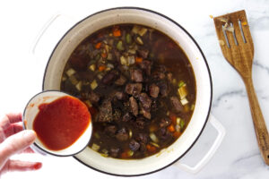 Adding tomato paste to a pot of beef soup.