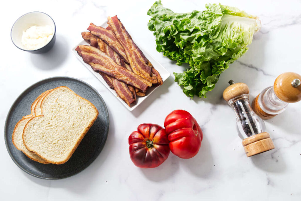 BLT sandwich ingredients with bacon, lettuce, tomatoes, mayonnaise, and toasted bread.