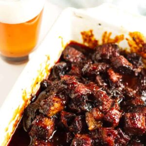 Crispy brisket burnt ends in a white dish, amber beer behind.