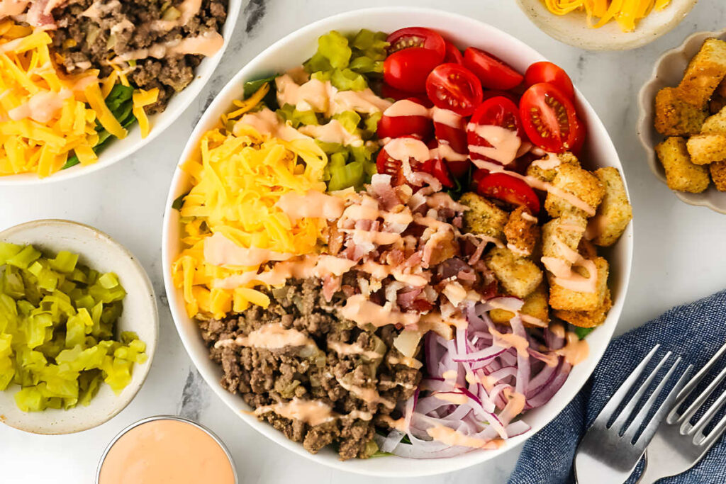 Bowl of ground beef salad with cheese, veggies, bacon, and creamy dressing.
