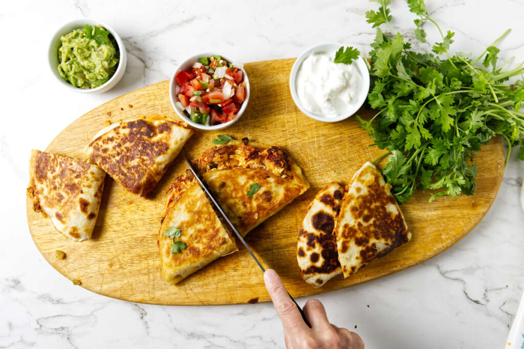 Slicing quesadillas in half on a cutting board.