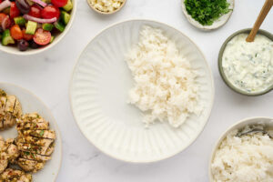 Greek chicken bowls with lemon rice, vegetables, feta cheese, and herbs.