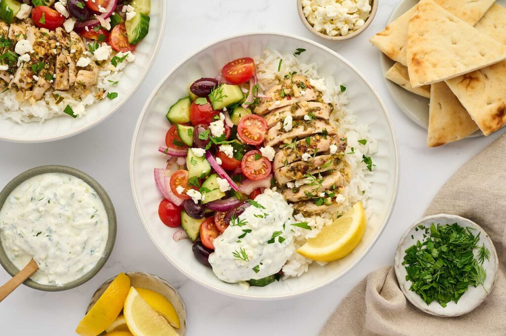Assembled Greek chicken rice bowl with tzatziki and fresh herbs.