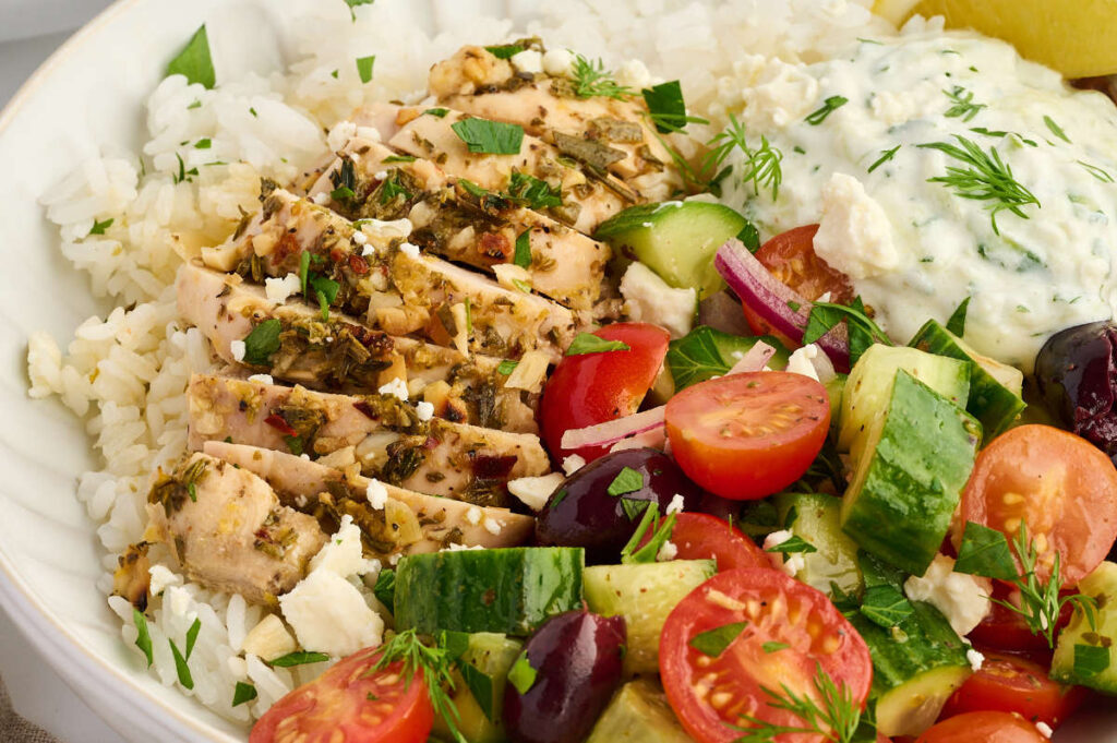 Greek chicken bowl served with warm pita bread and lemon wedges.